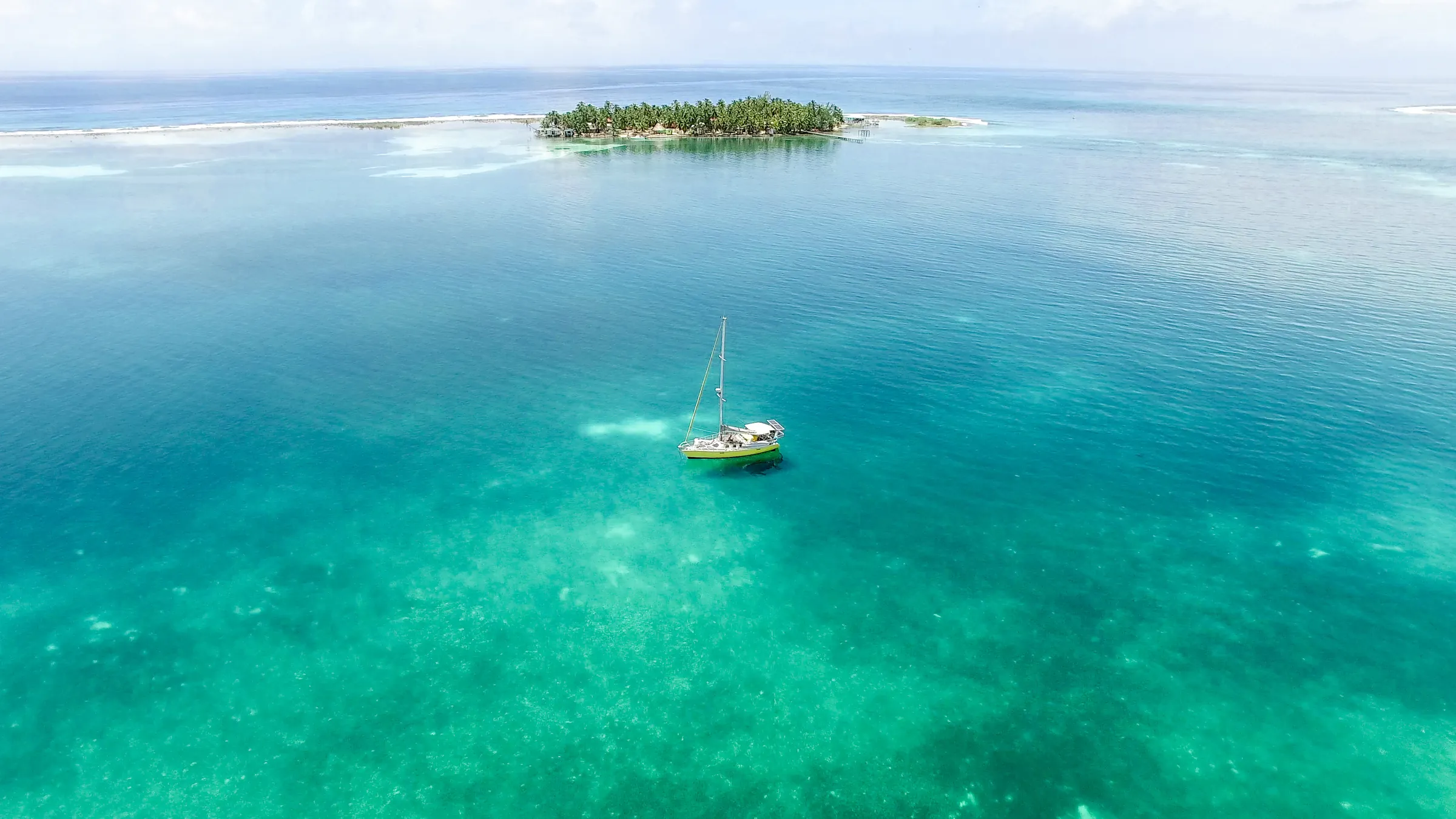 Sailboat in turquoise water beside a small caye, Belize