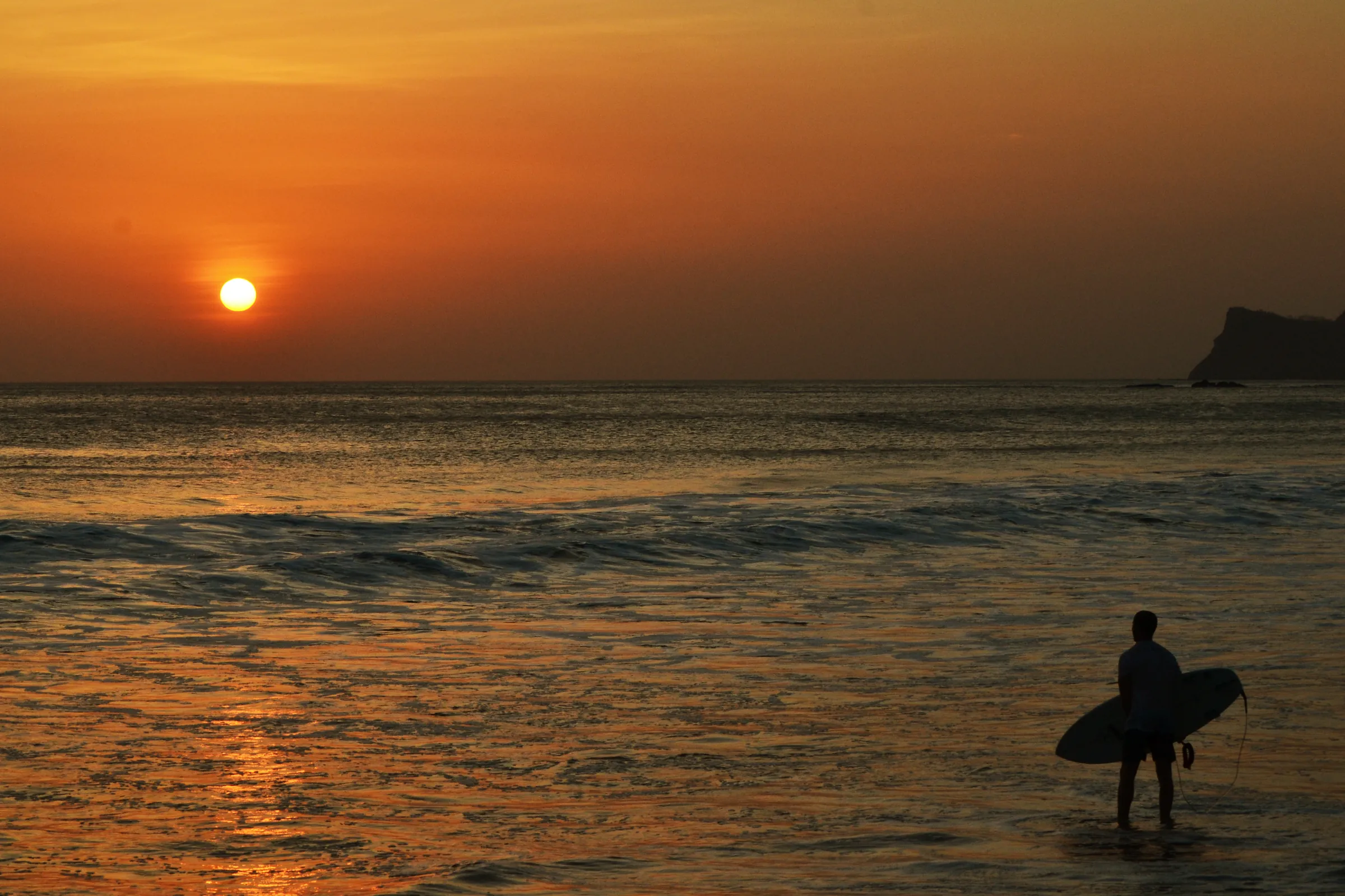 Surfer silhouetted against an orange sunset, Nicaragua