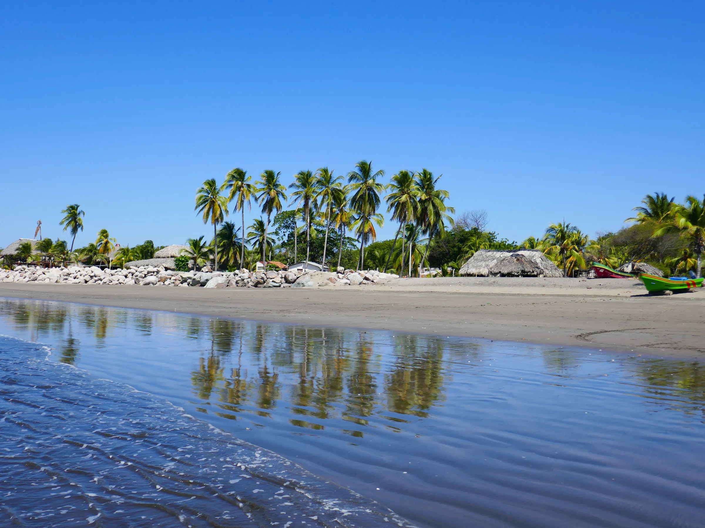 Palms and fishing pangas reflected on a wet sand beach, Nicaragua