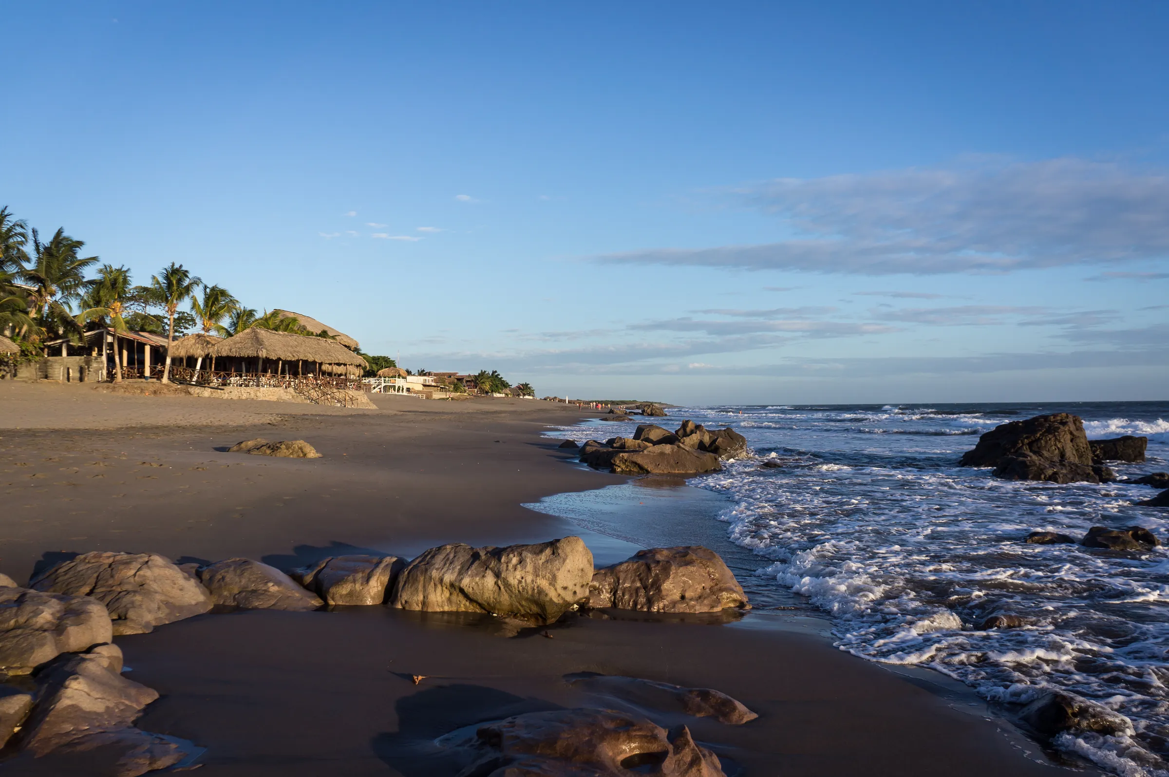 Dark sand beach with rocks and palm-thatched huts, Nicaragua