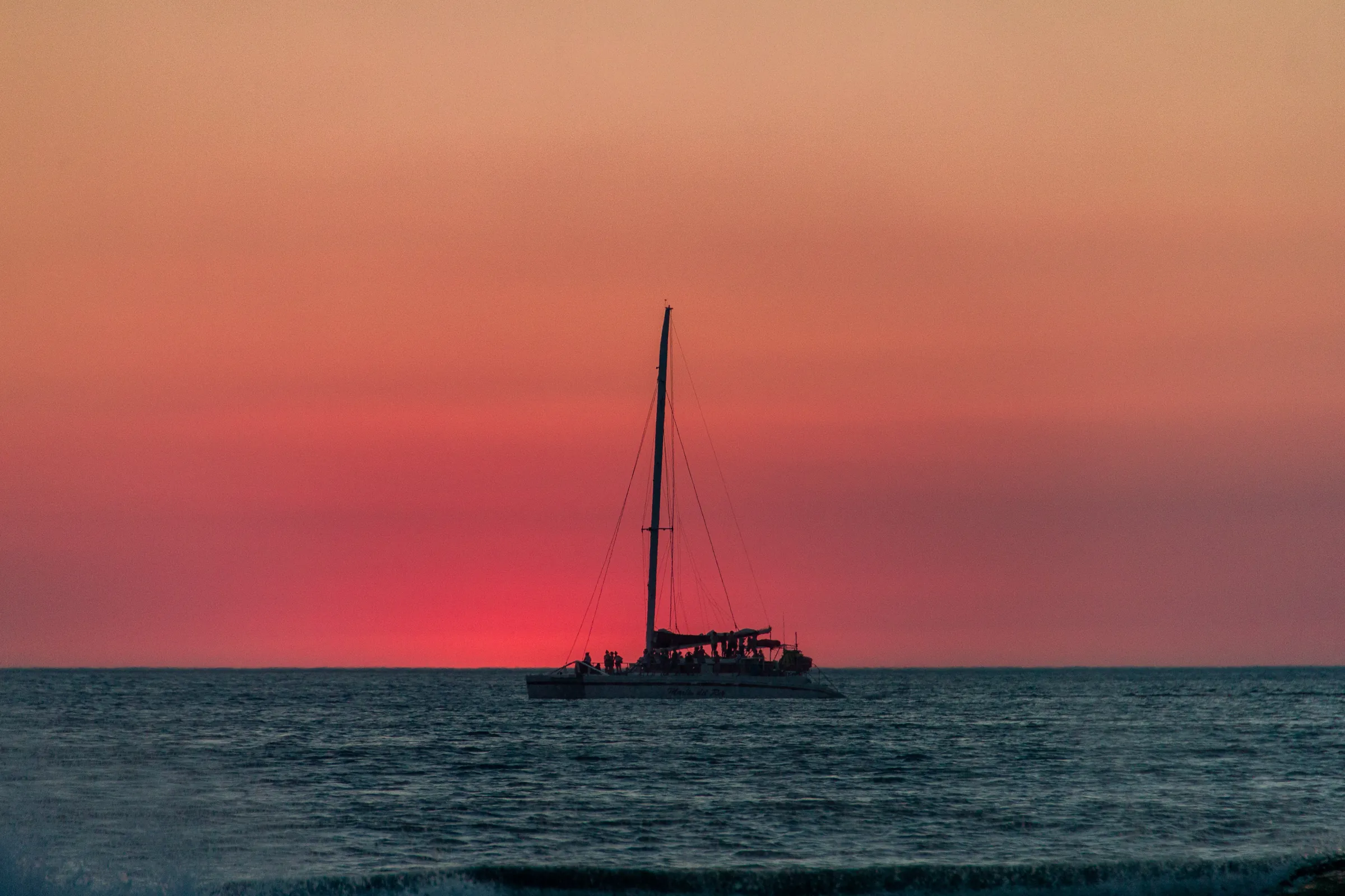 Sailboat silhouetted beneath a pink sunset