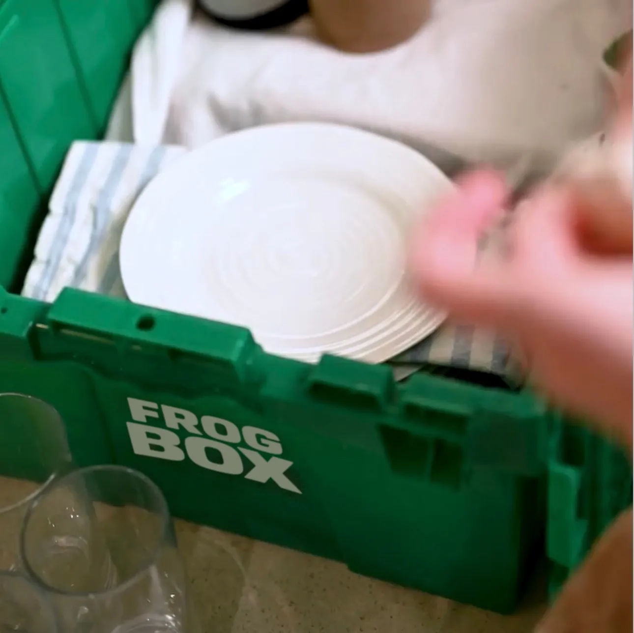 Close-up of dishes being packed into a green bin with Frogbox branding