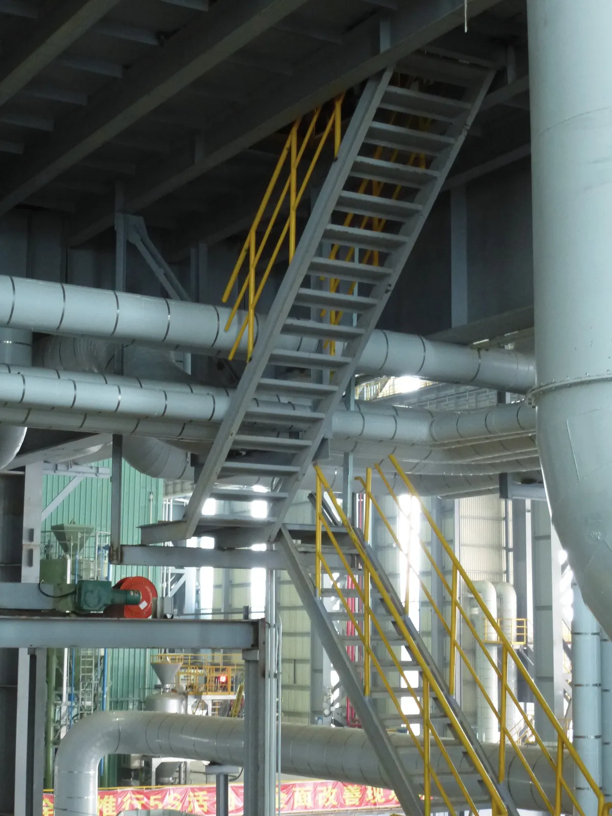 A pipe crosses a metal staircase inside an industrial plant.