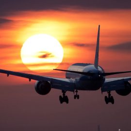 A boeing 777 plane flying into the sunset