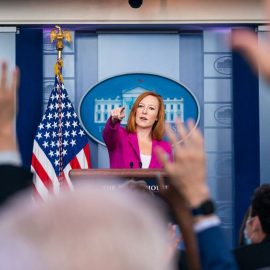Jen Psaki pointing at journalists raising hands in the White House briefing room.