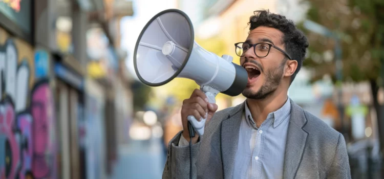 a young man wearing glasses speaking into a megaphone on a city street illustrates how to get customers for a new business