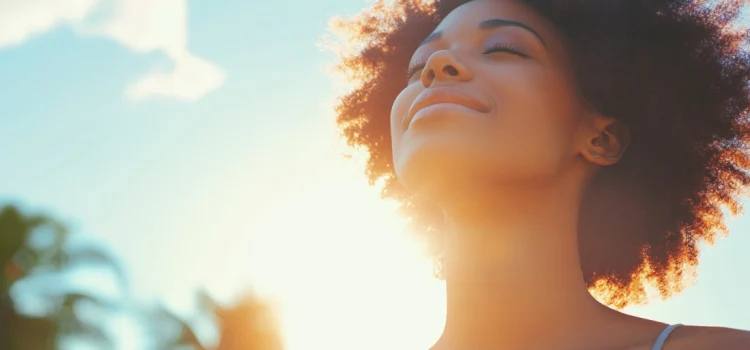 The 3 Sunlight Hormones That Affect How You Sleep A woman feeling sunlight hormones with her eyes closed outside
