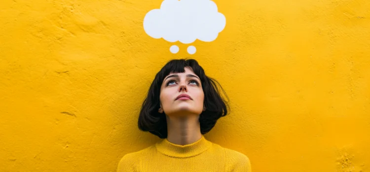 How to Keep an Open Mind When Life Throws Curveballs A woman keeping an open mind in front of a yellow wall with an empty thought bubble