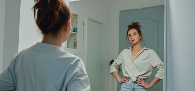 What Is Self-Esteem, and Why Is It Important? A woman looking in the mirror and her hands on her hips depicts the question "What is self-esteem, and why is it important?"