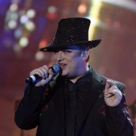 Boy George singing on stage and wearing a black hat with glitter