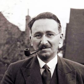 Friedrich Hayek (socialism critic) smoking a pipe with buildings in the background