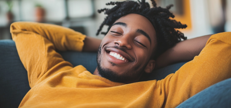 A man happily laying on the couch and realizing that laziness is good