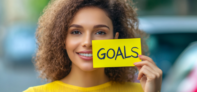 A woman holding up a sticky note that says "GOALS" as she learns how to set personal goals