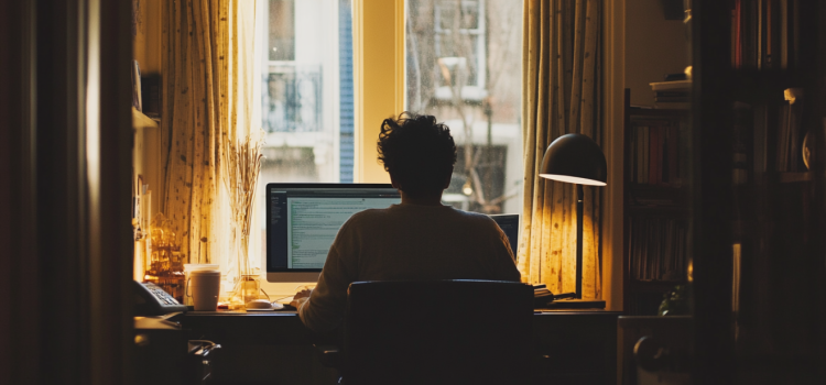 A remote worker sitting at a desk in his home office in front of a window