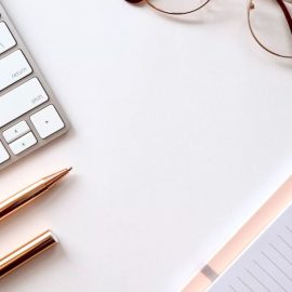 A clean and organized desk with a notebook, pens, keyboard, and glasses