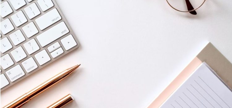 A clean and organized desk with a notebook, pens, keyboard, and glasses