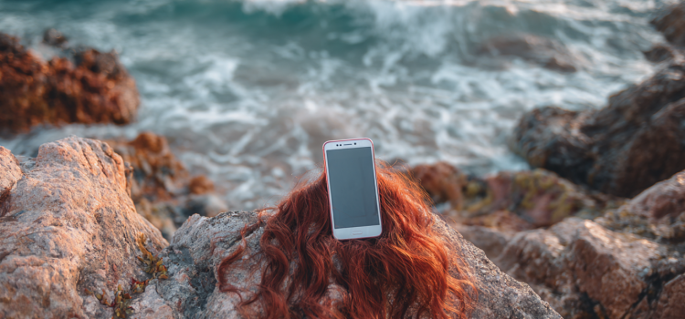 The Sirens’ Call by Chris Hayes—Book Overview & Takeaways A cell phone with long red hair sitting on a rock in the ocean like a siren