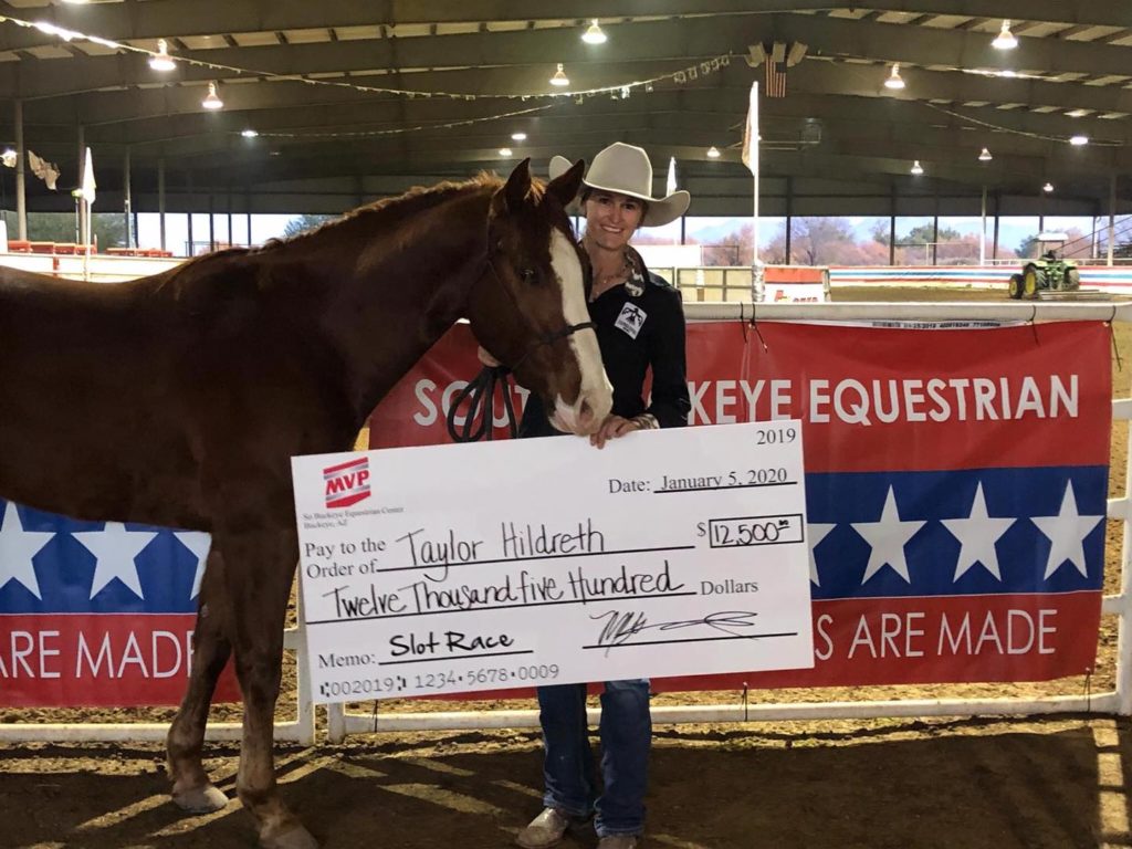 Taylor Hildreth standing next to a sorrel horse holding a large check