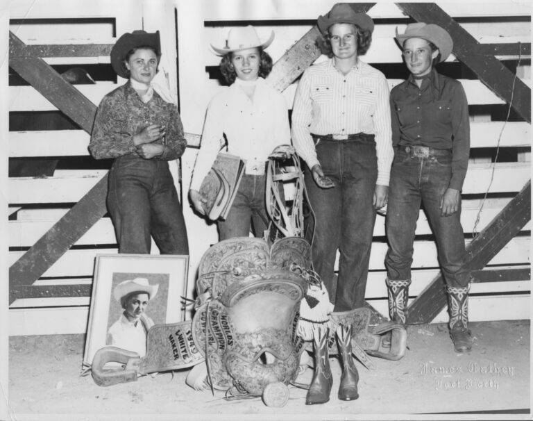 1949 Girl's Rodeo Association champions stand shoulder to shoulder behind their prizes, including a trophy saddle and boots.