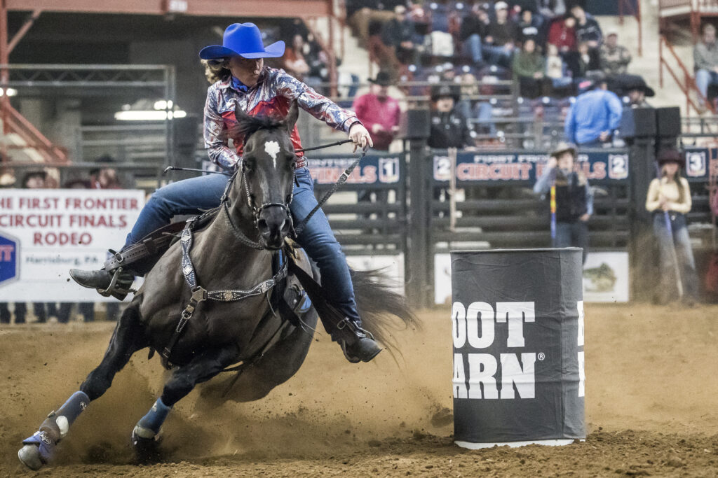 Willie Horzepa turns a barrel in a blue hat on her black horse Diva