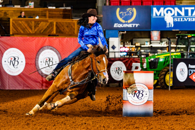 heidi Gunderson sits on a horse turning a barrel in a blue shirt