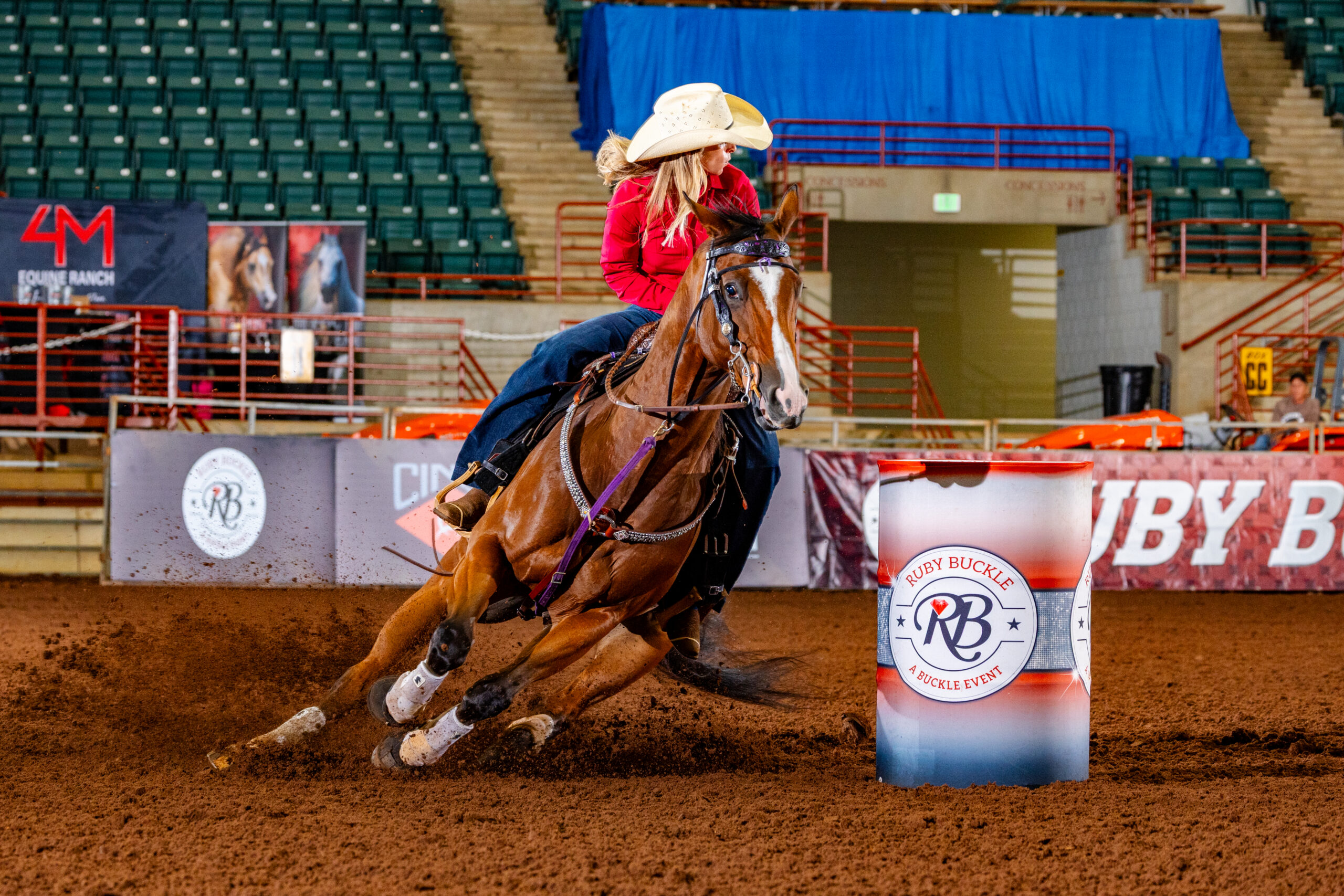 Blaise Wheeler turns a barrel in a red shirt on her bay horse