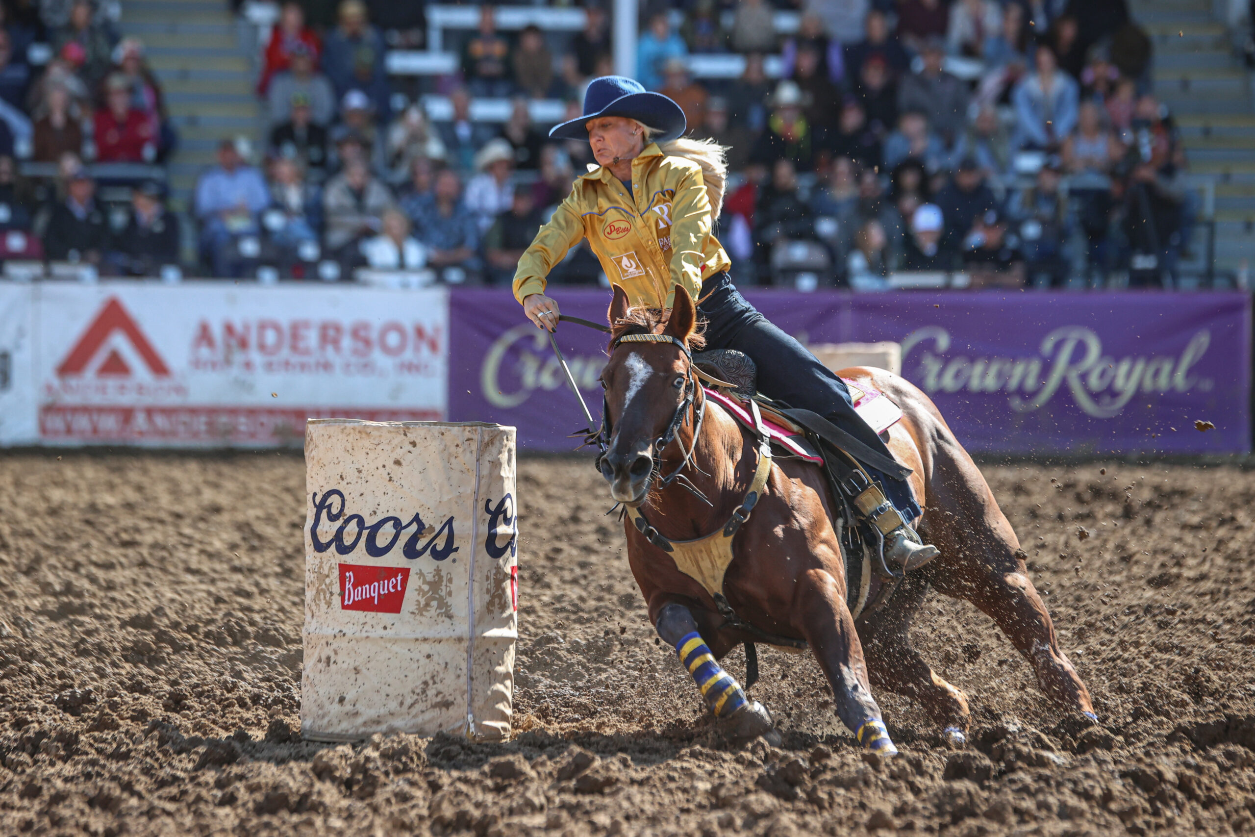 Summer Kosel turns a barrel in a yellow shirt in the mud on her horse