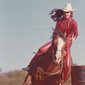 a woman in red pants and a white cowboy hat and red shirt sits on a horse turning a barrel