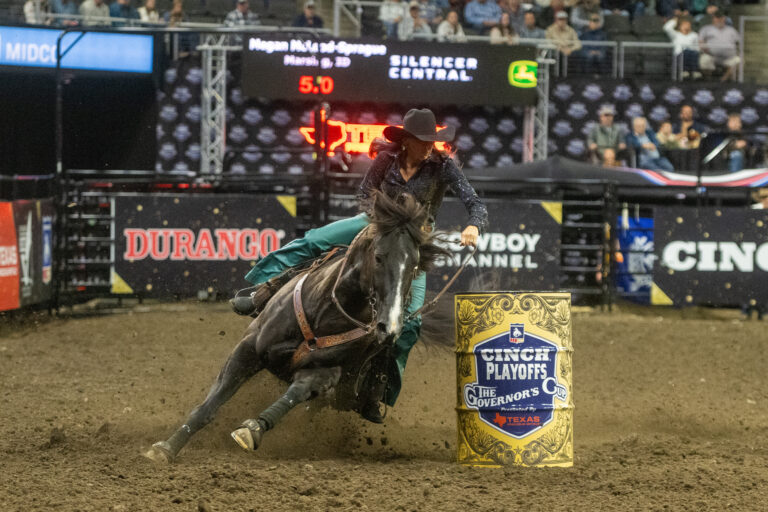 A woman in blue pants turns a barrel on a black horse