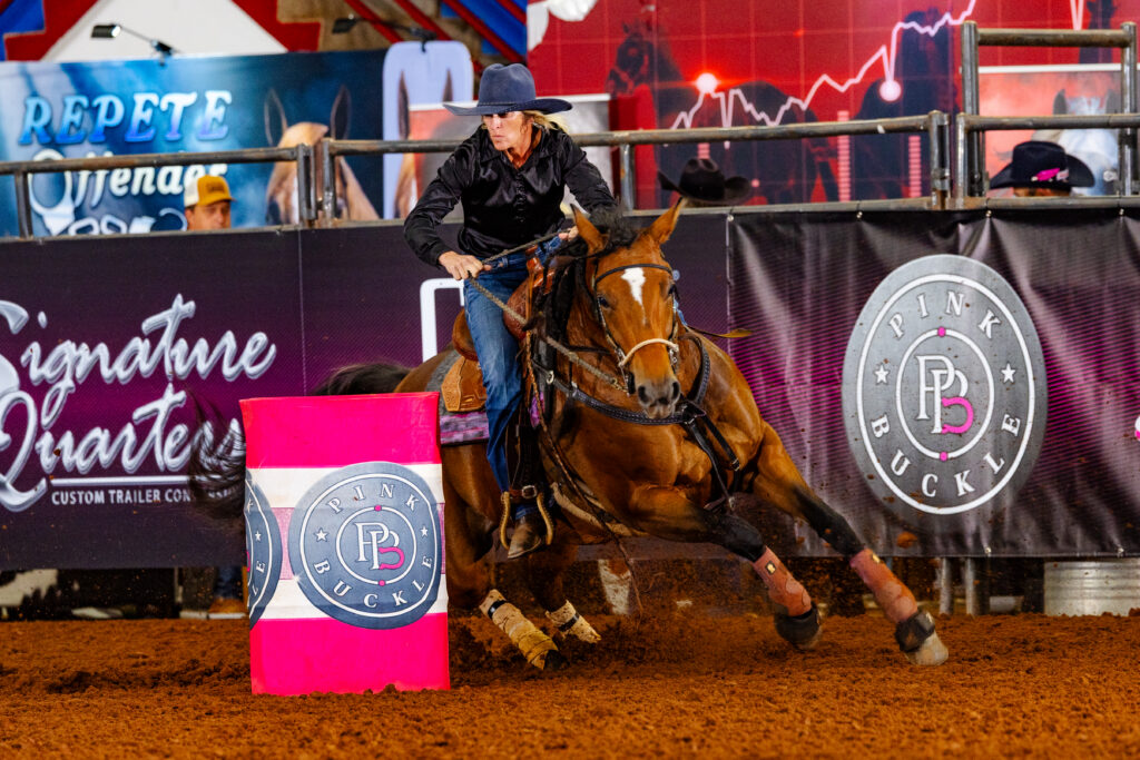 Alona James turns a barrel with two hands on the reins on her dark mare