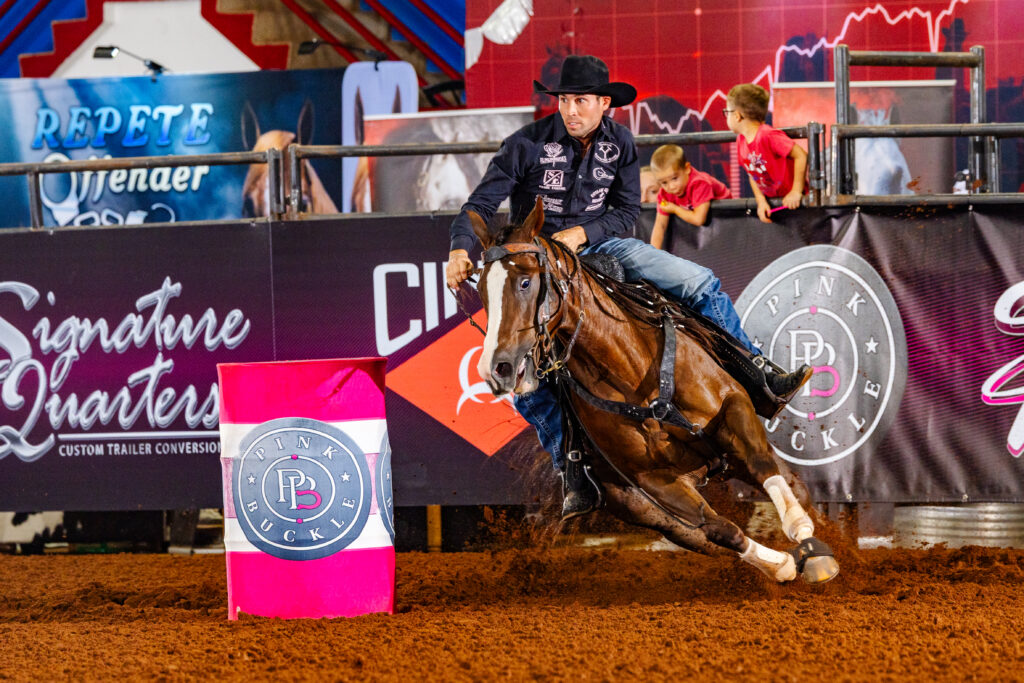 A man turns a Pink Buckle barrel on a dark horse