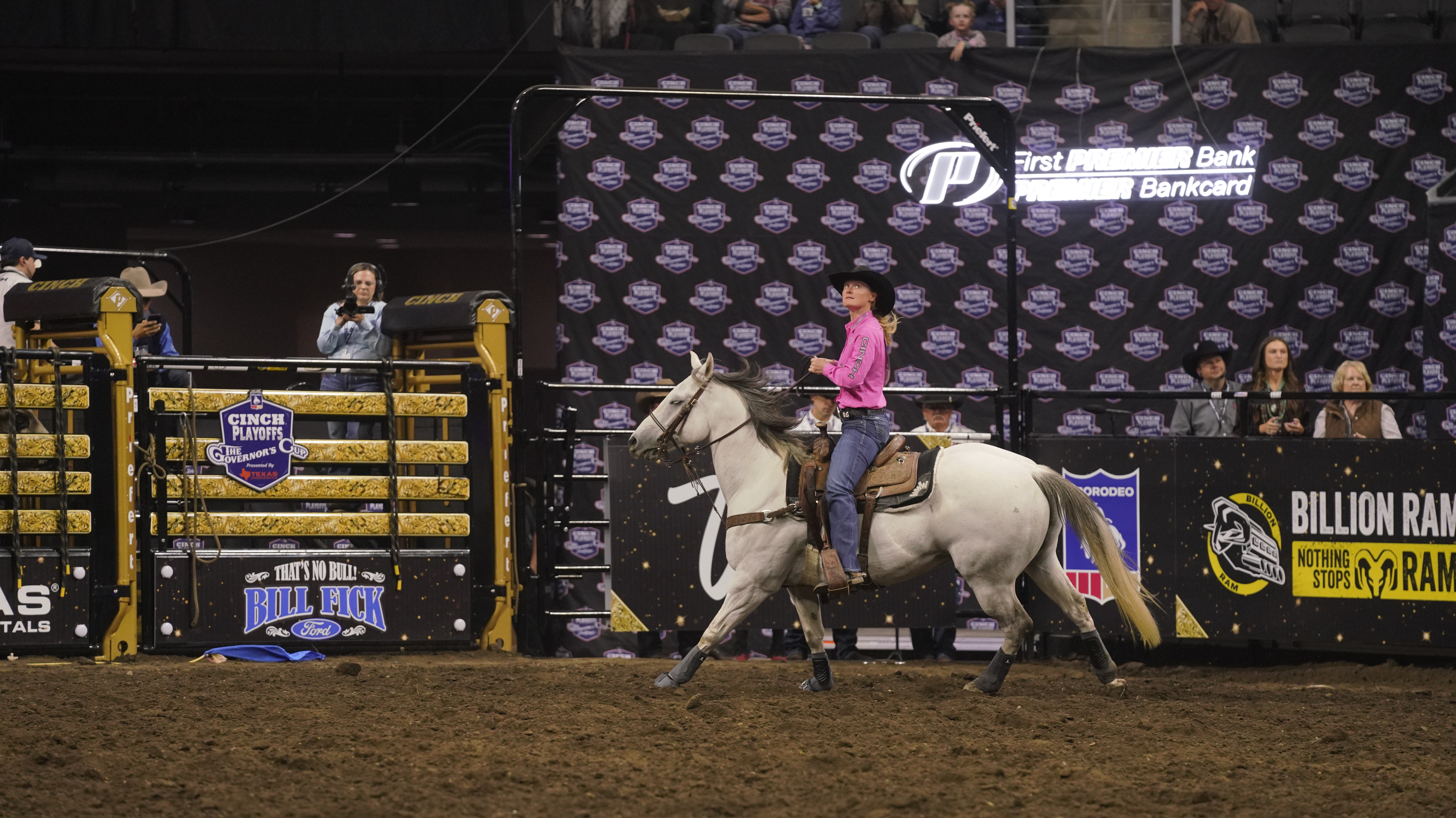 A girl in a pink shirt looks up at the scoreboard on a grey horse