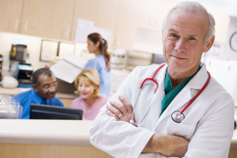 Smiling doctor with arms crossed and nurses at reception