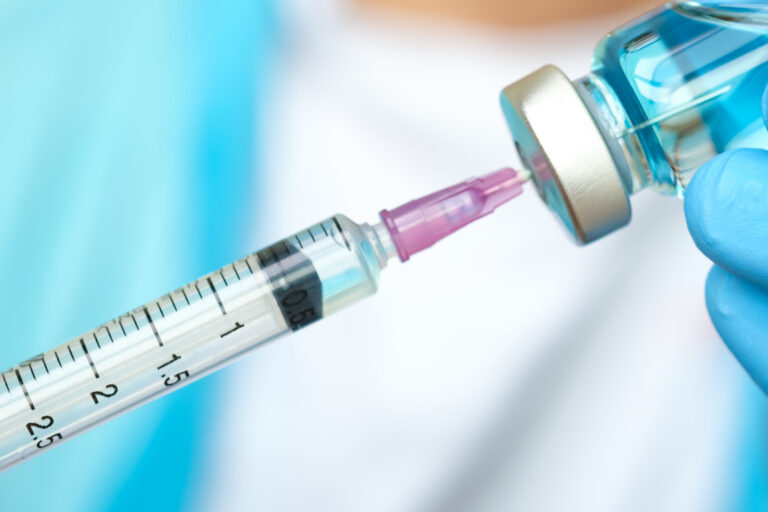 doctor's hand holds a syringe and a blue vaccine bottle at the hospital. Health and medical concepts