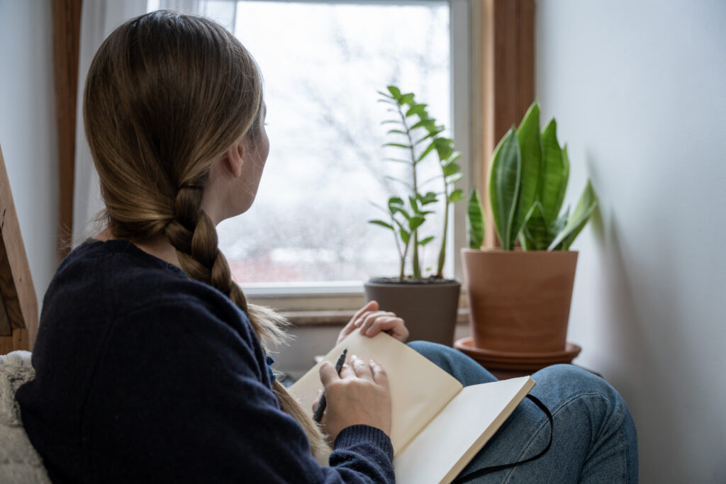 Woman staring out the window while journaling.