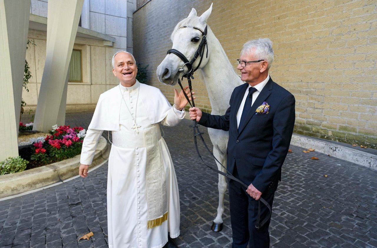 Pope in white smiles with man in business suit and gray horse in between them