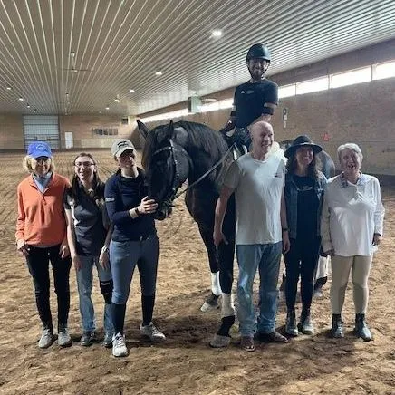 Group of people standing with horse and rider in indoor arena