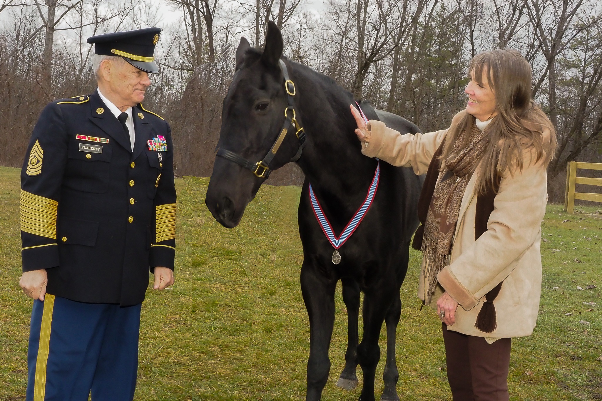 Image of dark horse standing with woman petting his neck and a US Army officer also standing next to him