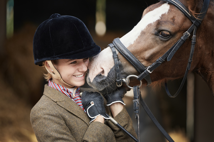 Helmeted English rider gtes nuzzle from bridled horse with blaze face