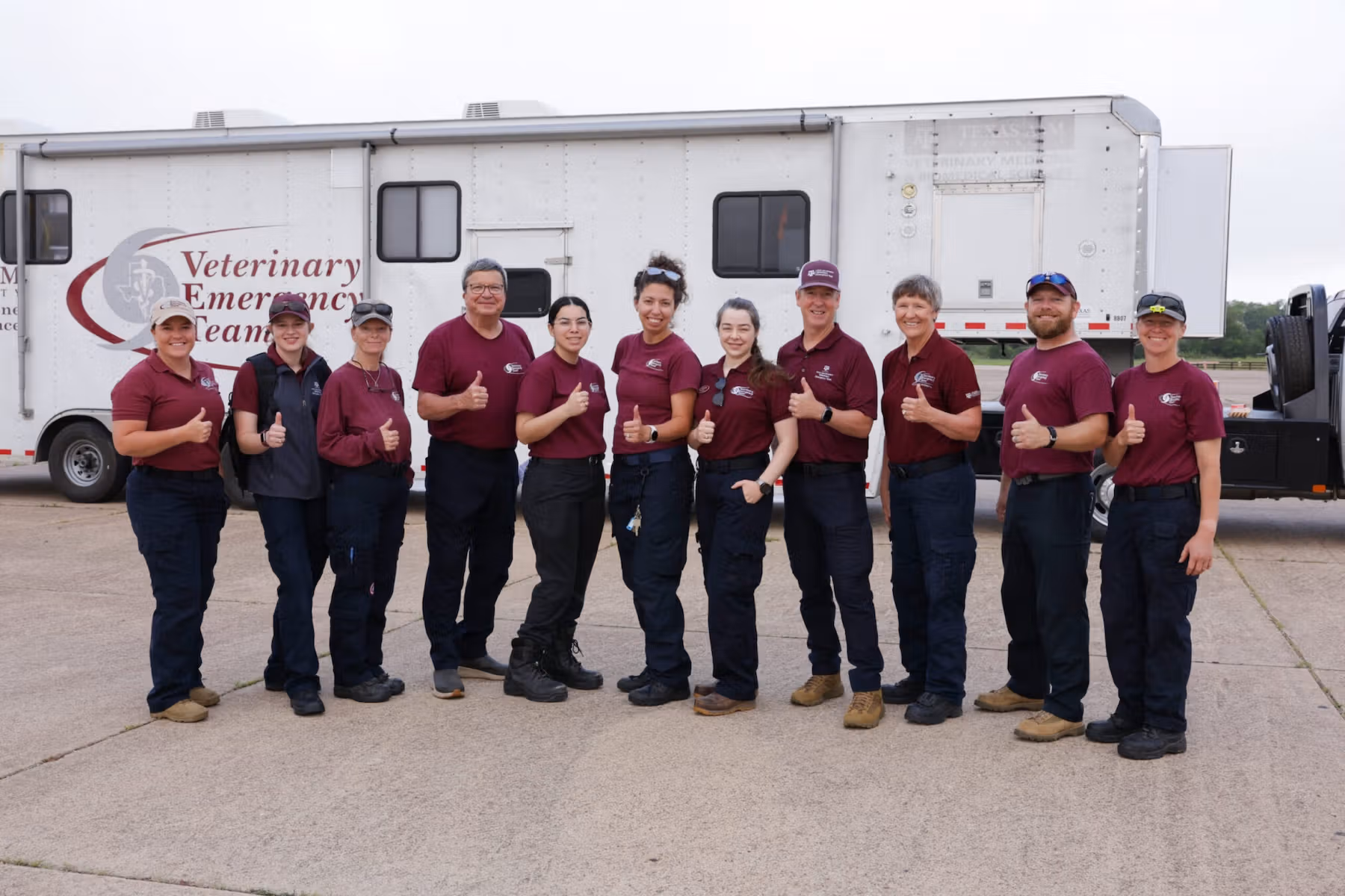 A group of people giving the "thumbs up" sign in front of a mobile veterinary vehicle