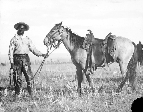 Black cowboy holding horse in Western tack in historic black and white image