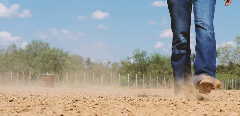 Cowgirl in cowboy boots walking through outdoor arena during sum