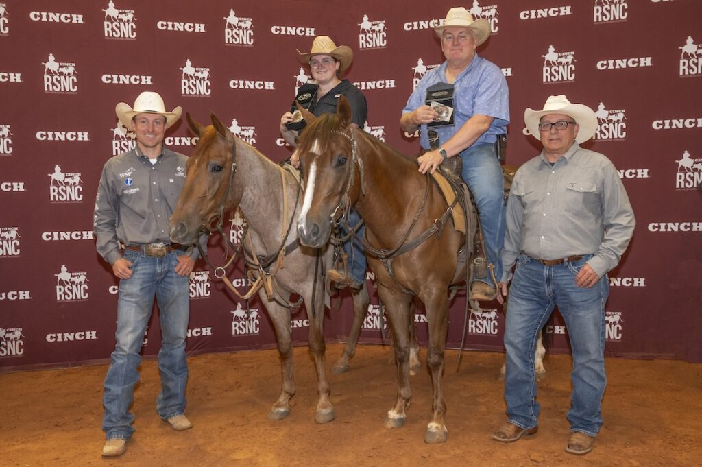 Logan Weldon and Mike Weldon hold trophy buckles on roan and sorrel horses, posed in front of backdrop.
