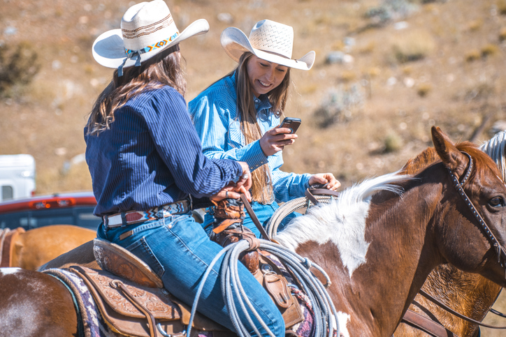 Two Female Western Ranchers Talk and Share Phone Pics on Horseback