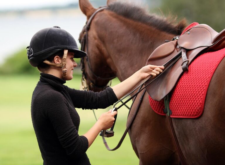 A woman checks her stirrup leathers before getting on a horse