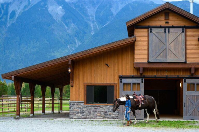 A woman leads a paint horse in western tack out of the barn