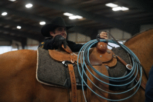 Patrick Smith standing behind a saddled roped horse, with one hand on the horn and one hand on the cantle.
