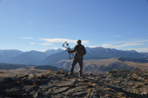 silhouette of man with bow on top of mountain, overlooking view of mountains