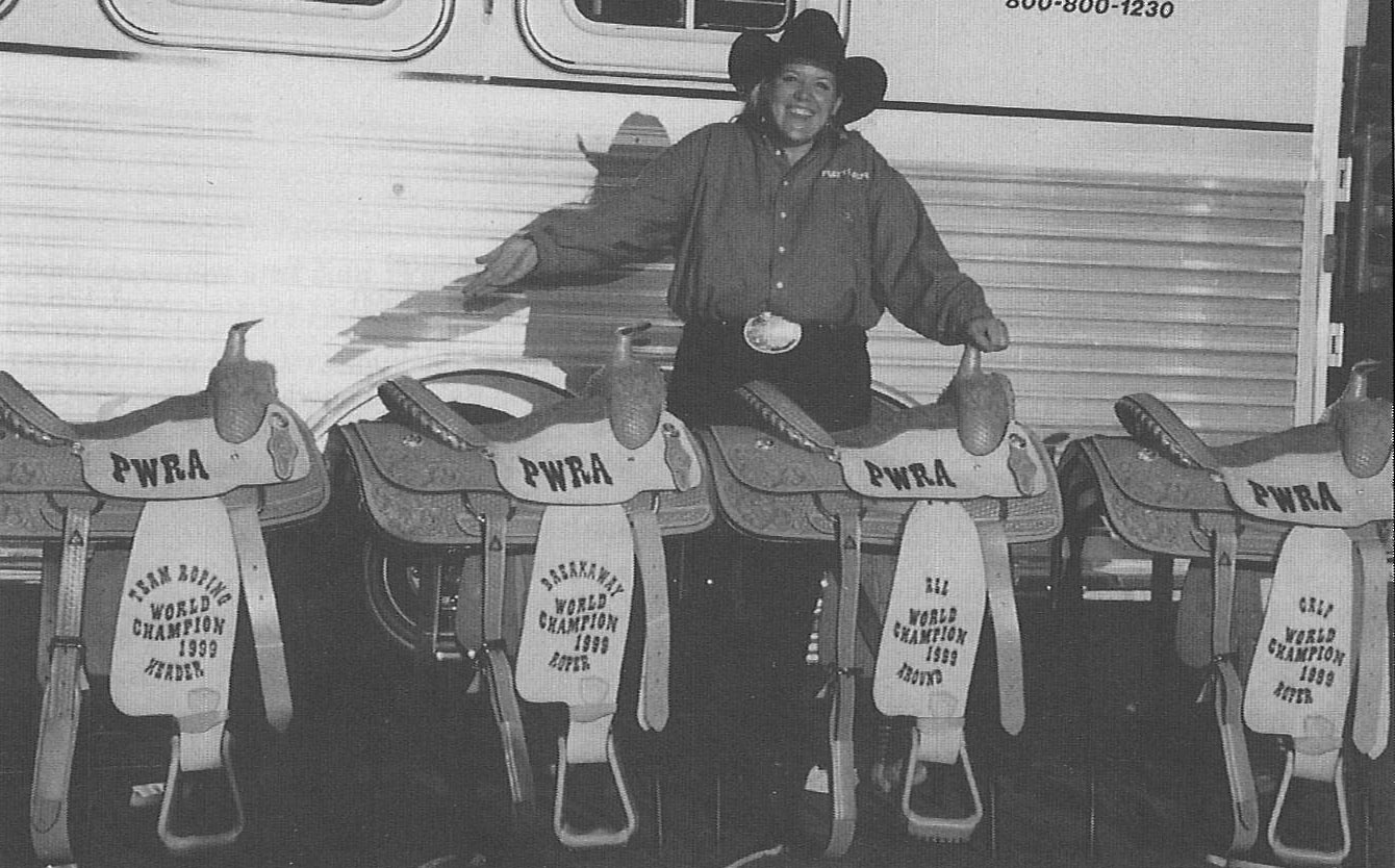 JJ Hampton standing behind a line of trophy saddles.