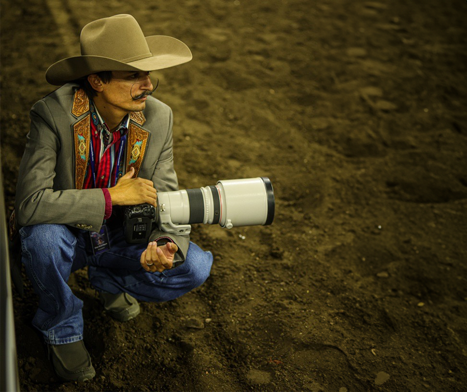 Photographer Clay Guardipee crouched in arena dirt with camera in hand.